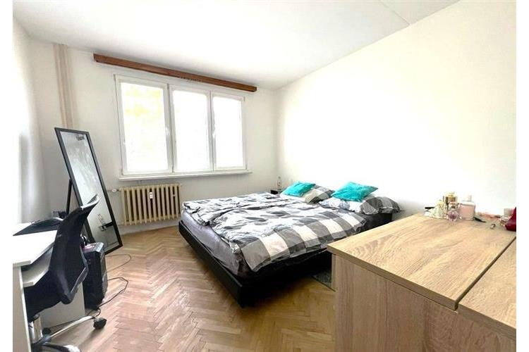 Světlá ložnice s parketovou podlahou, velkými okny a moderním nábytkem, nabízí komfortní prostor pro odpočinek a relaxaci.