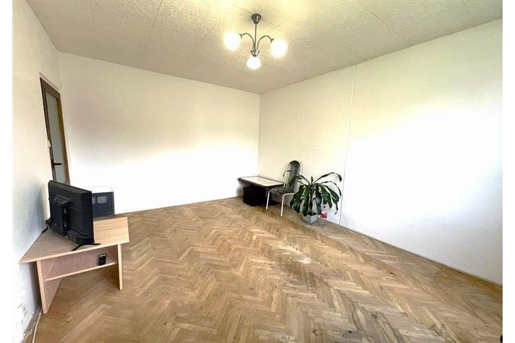 Světlý obývací pokoj s parketovou podlahou, neutrální stěny, moderní osvětlení a minimalistický nábytek vytvářejí útulný prostor.