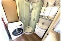 Kompaktní koupelna s moderní sprchou, praktickými úložnými skříňkami a dřevěnou podlahou. Vybavená pračkou pro komfortní bydlení.