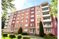 Bytový dům s moderní fasádou, velkými okny a balkóny, v klidné rezidenční čtvrti, ideální pro rodinné bydlení.