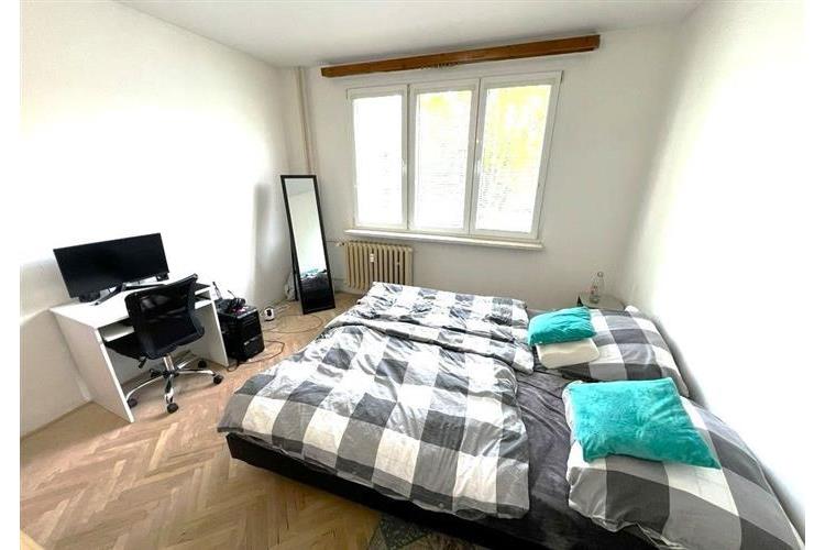 Světlá ložnice s parketovou podlahou, velkým oknem a moderním pracovním koutkem, ideální pro pohodlné bydlení.