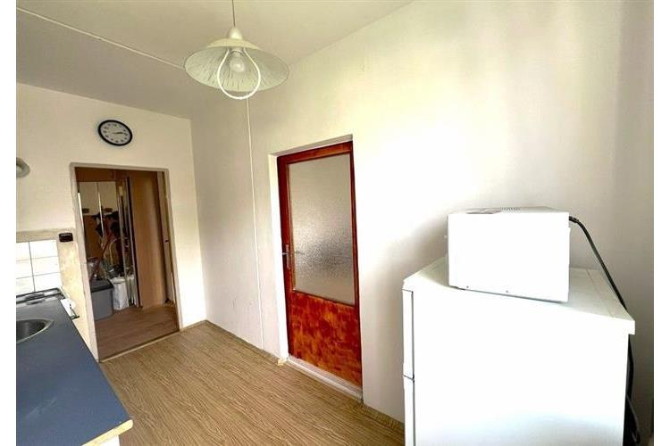 Úzká kuchyně s dřevěnou podlahou a bílými stěnami, obsahuje lednici a mikrovlnnou troubu, moderní styl, dveře s matným sklem