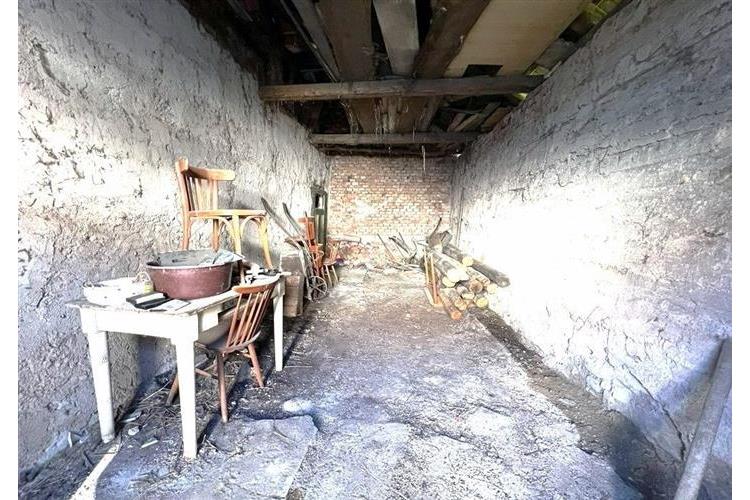 Prázdný sklepní prostor s odkrytou cihlovou stěnou, potřebující rekonstrukci, vhodný pro skladování dřeva nebo úložné účely.
