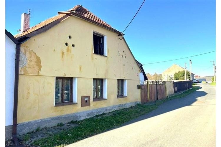 Starší rodinný dům s šikmou střechou, žlutá fasáda, dřevěná okna, klidná lokalita v malebném venkovském prostředí.