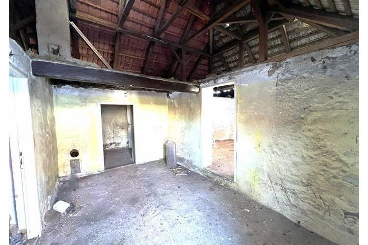 Neudržovaný interiér s odhalenými trámy, kamenné stěny a dřevěná střecha, vhodné pro rekonstrukci nebo přestavbu na moderní prostor