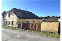 Starší venkovský dům s šikmou střechou, kamennou fasádou a dřevěnou bránou, vhodný k rekonstrukci v klidné lokalitě.