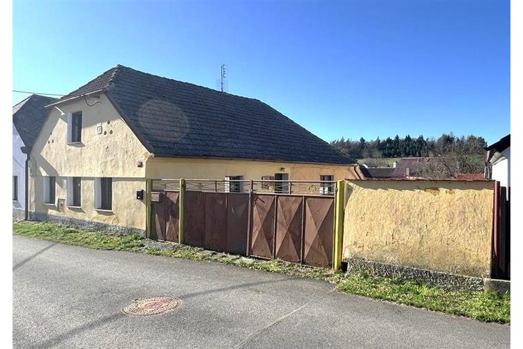 Starší venkovský dům s šikmou střechou, kamennou fasádou a dřevěnou bránou, vhodný k rekonstrukci v klidné lokalitě.