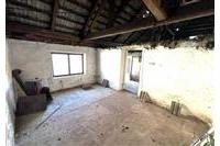 Podkrovní místnost s dřevěnými trámy a betonovou podlahou, vhodná k rekonstrukci, má velké okno poskytující dostatek přirozeného světla.