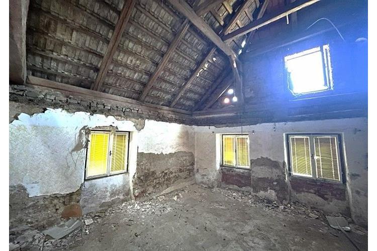 Podkrovní prostor se šikmým dřevěným stropem, původní zdivo a malá okna, vhodný pro rekonstrukci nebo modernizaci.