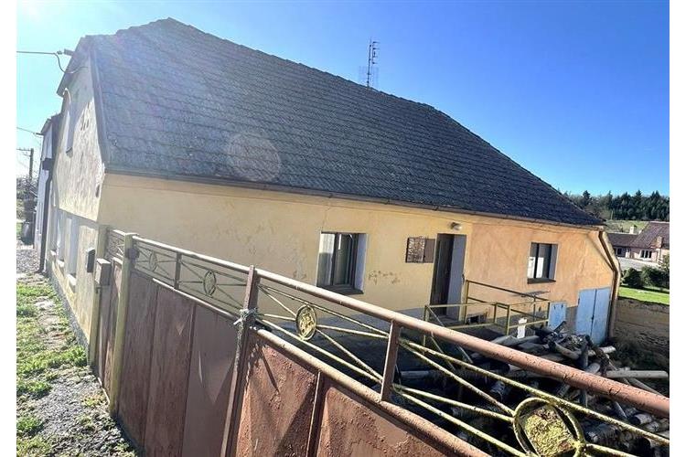 Starší venkovský dům s šikmou střechou, původní fasádou a kovovým plotem, umístěný na klidném místě s výhledem na okolní krajinu.