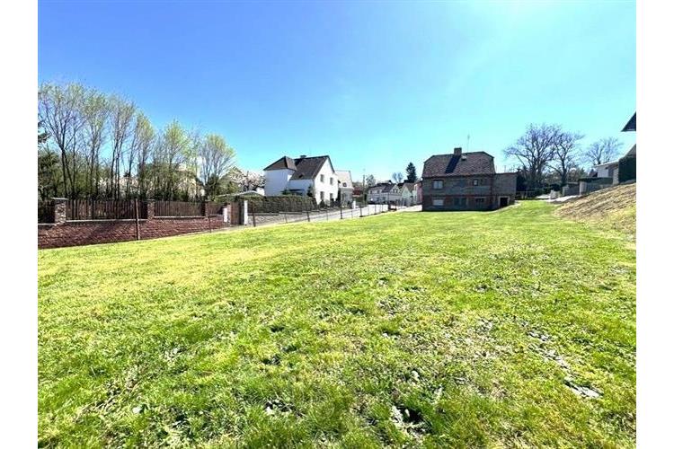 Rozlehlá travnatá zahrada s plotem, obklopená rodinnými domy, nabízí výhled do klidné rezidenční čtvrti v moderním stylu.