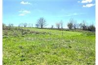 Volný stavební pozemek s travnatým pokryvem a výhledem na okolní krajinu, ideální pro výstavbu rodinného domu, klidná lokalita