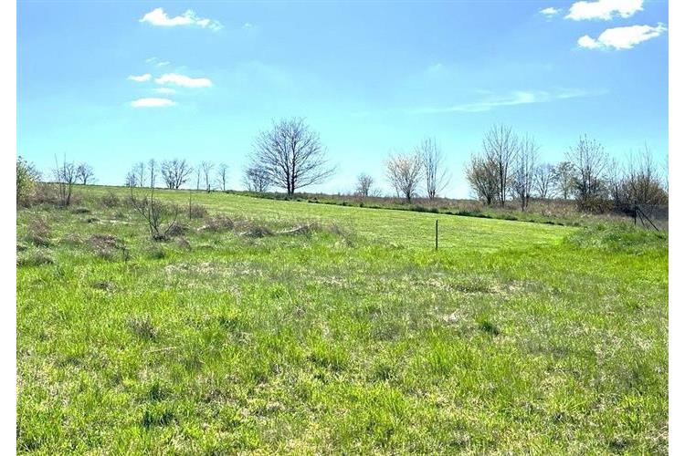 Volný stavební pozemek s travnatým pokryvem a výhledem na okolní krajinu, ideální pro výstavbu rodinného domu, klidná lokalita