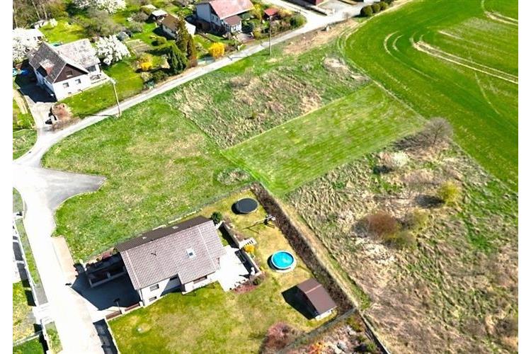 Prázdný stavební pozemek s travnatým povrchem v klidné lokalitě, ideální pro výstavbu rodinného domu, výhled do okolní krajiny