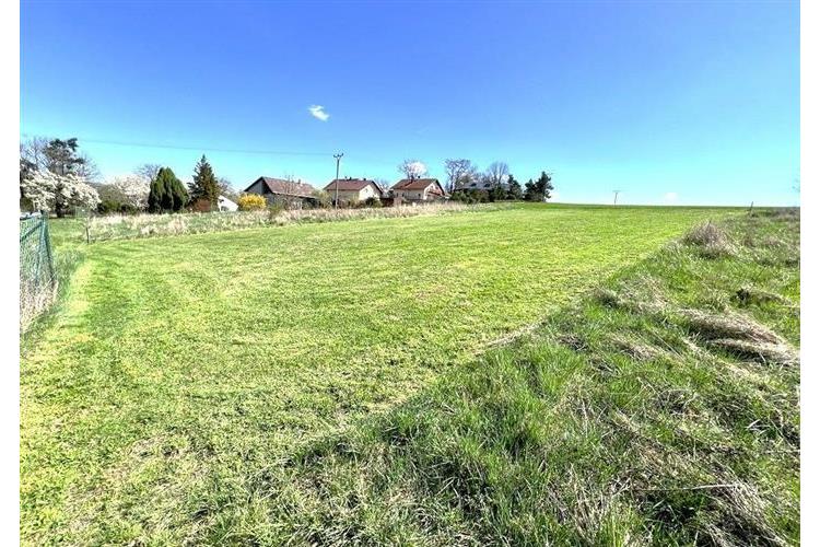 Plochý stavební pozemek s udržovaným trávníkem, ideální pro výstavbu. Klidná lokalita, obklopena přírodou a blízkostí obytných domů.