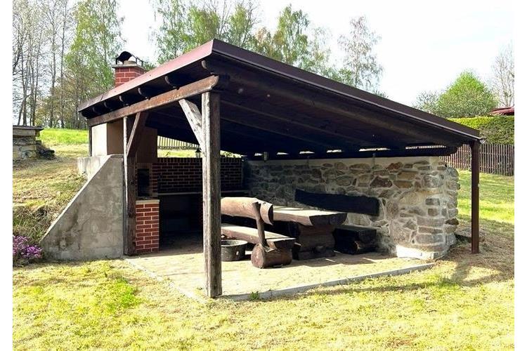 Zahradní altán s dřevěným posezením, kamennými zdmi a grilem, ideální pro venkovní aktivity a relaxaci na čerstvém vzduchu