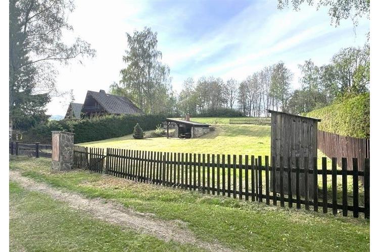 Rozlehlá zahrada s dřevěným plotem, travnatým terénem a okolní zelení, ideální pro rekreační využití nebo výstavbu venkovského domu.