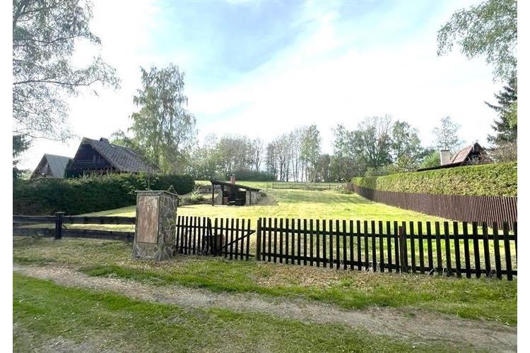 Rozlehlá zahrada s trávníkem, obklopená dřevěným plotem, ideální pro výstavbu. Klidné prostředí, blízko lesa, ideální pro rekreační účely.