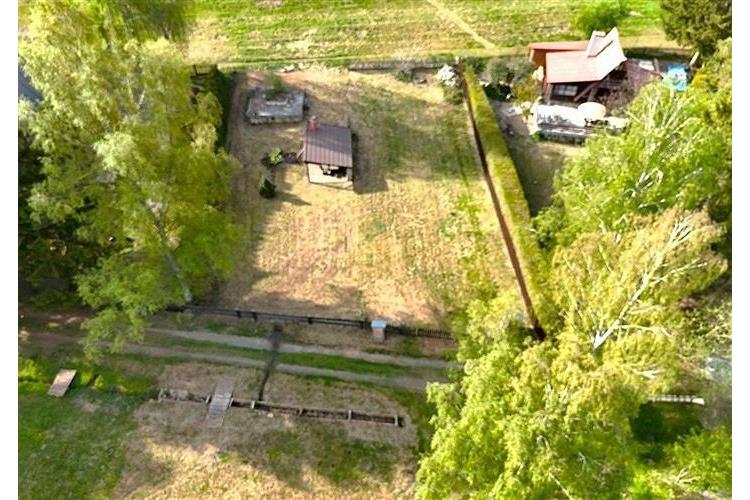 Zahrada s altánem a dřevěnou chatou na okraji pozemku, lemovaná zelení, nabízí soukromí a prostor pro relaxaci.